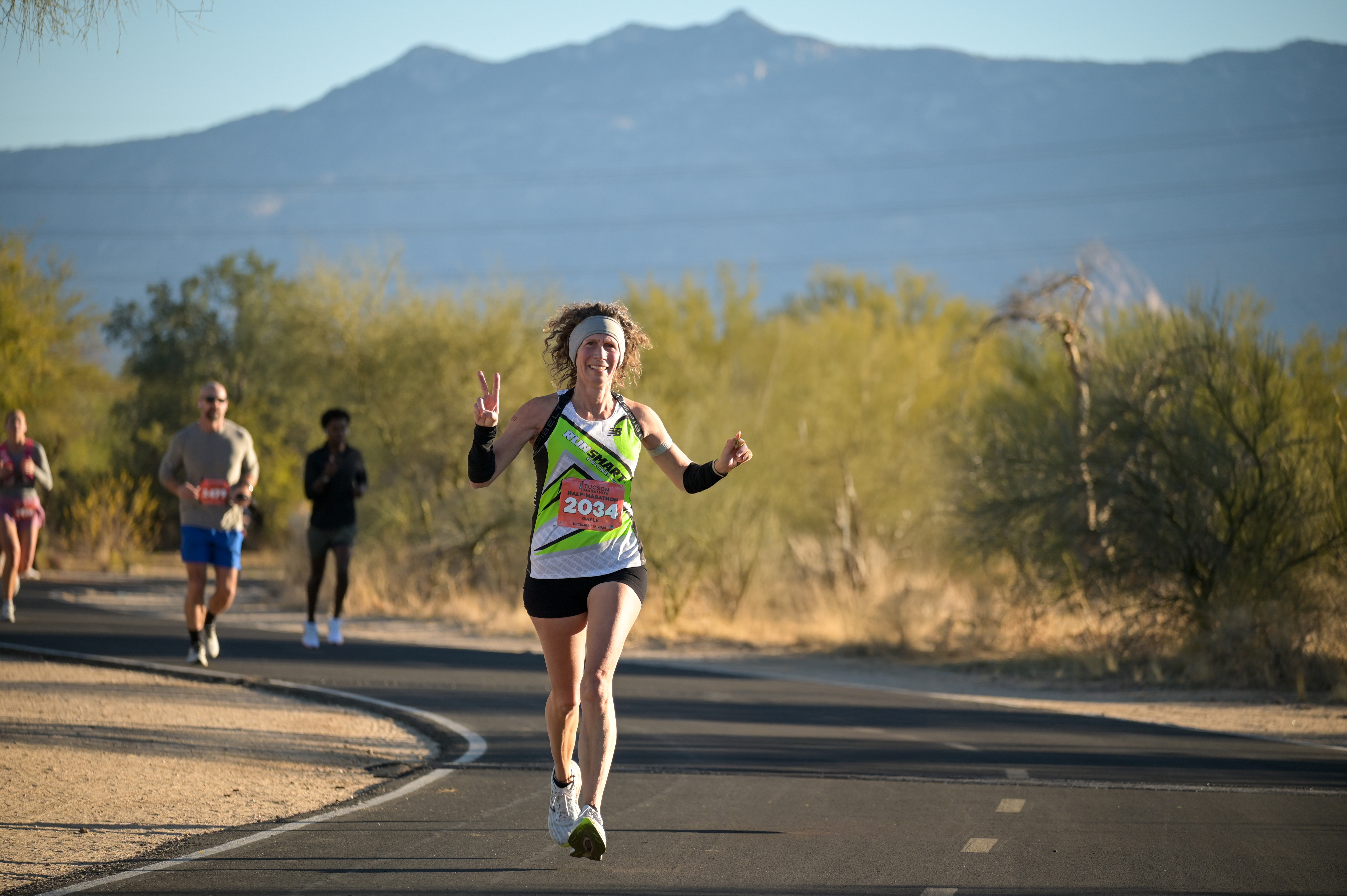 RunSmart runner Gayle racing with a smile and peace sign