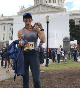 Carrie Sauber Waters smiling holding metal after a marathon